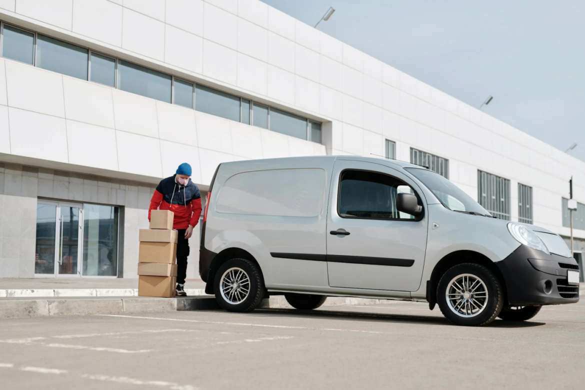 A delivery driver loading boxes into the back of a white van, preparing for daily deliveries.