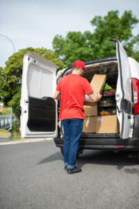 A delivery driver in a red shirt unloading boxes from a white van for a customer delivery.