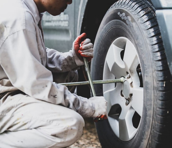 A mechanic tightening the bolts on a car tire outdoors.